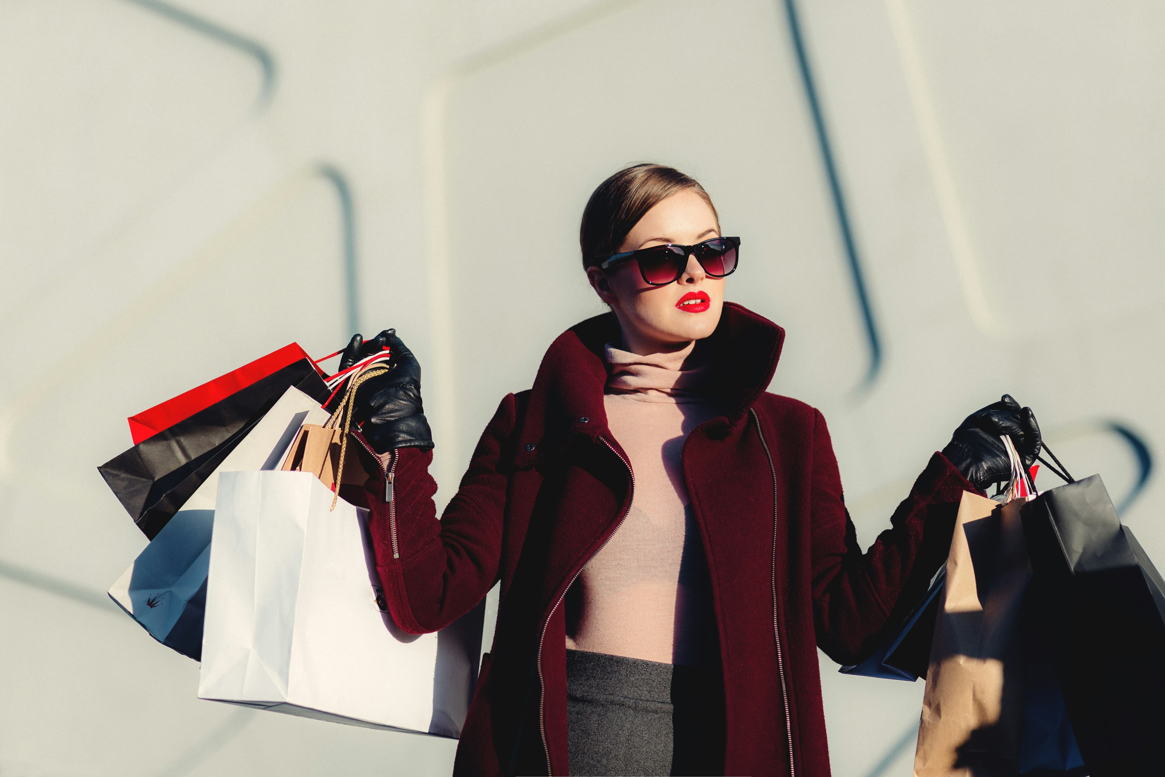 Fashion shopper in a burgundy coat holding multiple retail bags, representing real buyers behind the thousands of Shopify store product listings worth studying for product research